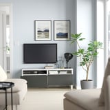 Living modern cu bancă TV albă BESTÅ, televizor cu ecran plat, decor și plante. Pereți albaștri deschisi, lumină naturală și decor minimalist.