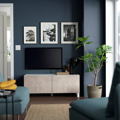 Living modern cu pereți albastru închis, suport TV BESTÅ din marmură deschisă, televizor cu ecran plat, plante verzi.