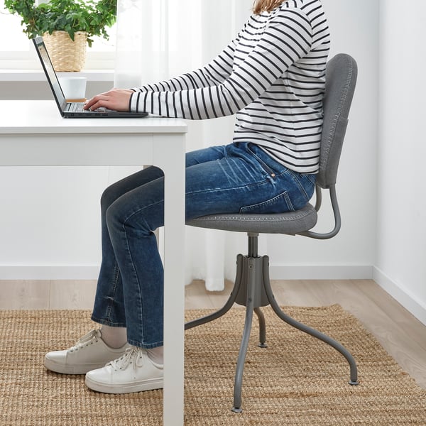 Persoană care stă pe un scaun BJÖRKBERGET, tastând pe un laptop la un birou alb. Scaunul are înălțime reglabilă și funcție de pivotare.