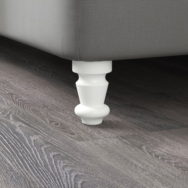 Mobilier tapițat gri cu picior ornamentat alb pe podea din lemn închis.