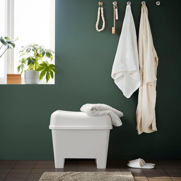 Un scaun de baie din plastic alb depozitează prosoape, stă lângă o plantă. Robust cu capac pentru depozitare ascunsă.