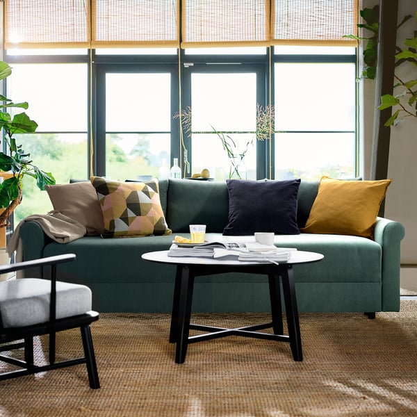 Living modern cu canapea extensibilă verde DÅNHULT, perne colorate și plante de fereastră.