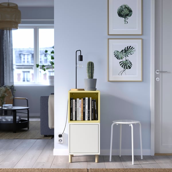 Living modern cu pereți albaștri, unitate EKET, cactus și imprimeuri artistice. Scaun alb în apropiere.