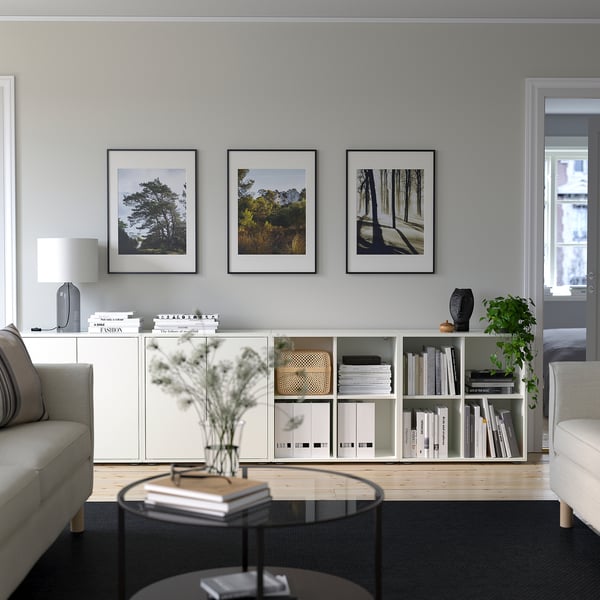 Living minimalist cu depozitare EKET, cărți, decor, fotografii din natură, măsuță de cafea rotundă, canapea gri și lumină naturală.