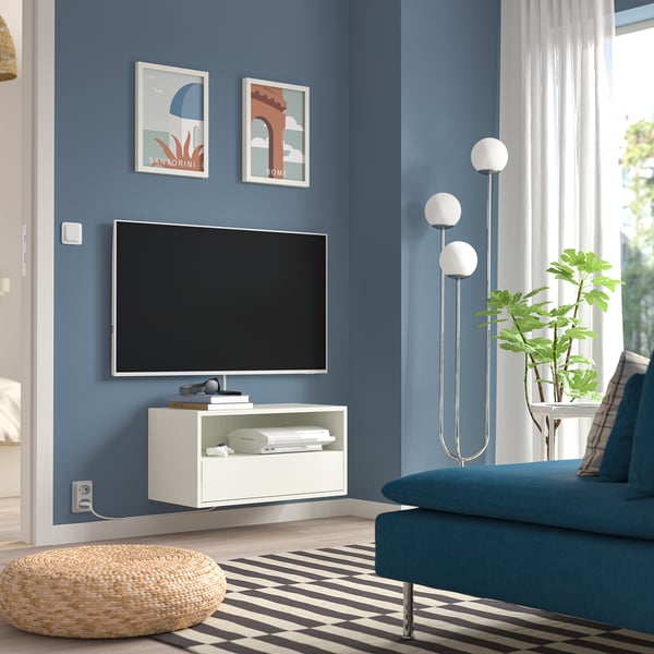 Living modern cu pereți albaștri, unitate TV EKETS, canapea albastră, covor alb-negru, lampă de podea, plantă în ghiveci și otoman.