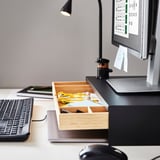 Configurație organizată a biroului cu tastatură, suport pentru monitor și sertar deschis care arată papetărie.