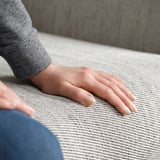 Persoană așezată pe o canapea gri texturată FAMMARP, cu mâinile sprijinite pe perne.