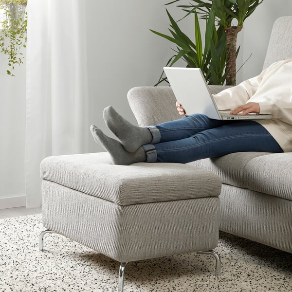 Persoană care stă pe canapea FAMMARP, folosind un laptop, cu picioarele ridicate pe scaun cu tetiere reglabile și depozitare.