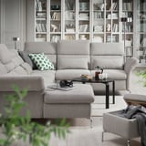 Living modern cu canapea gri FAMMARP, taburet, măsuță de cafea și raft plin de cărți și obiecte decorative.