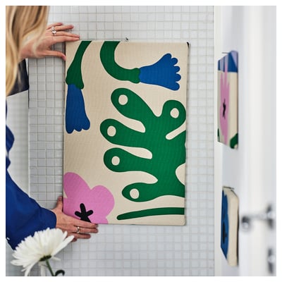 O persoană atârnă o țesătură colorată, abstractă pe peretele de gresie, probabil în scopuri decorative sau de cusut.