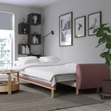 Canapea extensibilă albă, imprimeuri artistice, plantă în dormitor modern. Design curat cu rafturi și bancă roșie.