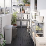Grădină balcon cu coșuri gri HÅLLBAR, rafturi albe, plante în ghivece și vedere la oraș.
