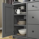 Dulap gri elegant HAUGA cu ușă deschisă care arată vase și căni albe stivuite. Design modern, finisaj gri robust, rafturi reglabile.