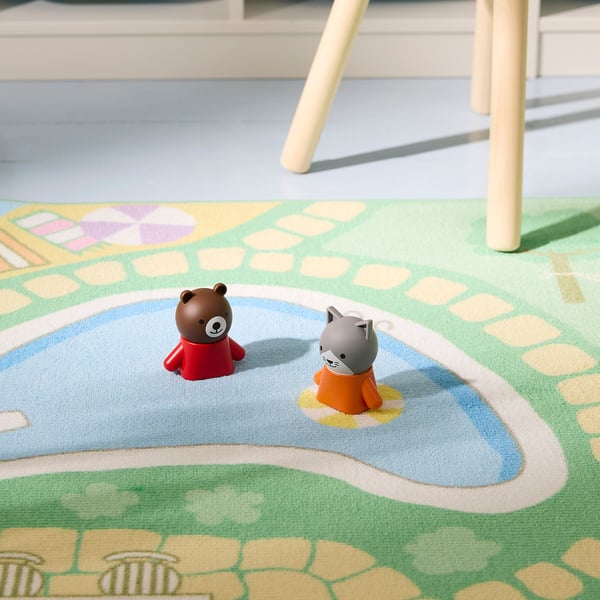 Două figurine de jucărie, un urs și o pisică, stau pe un covor de joacă colorat, cu modele. Covorul are un suport de cauciuc pentru a rămâne pe loc, prevenind alunecările.