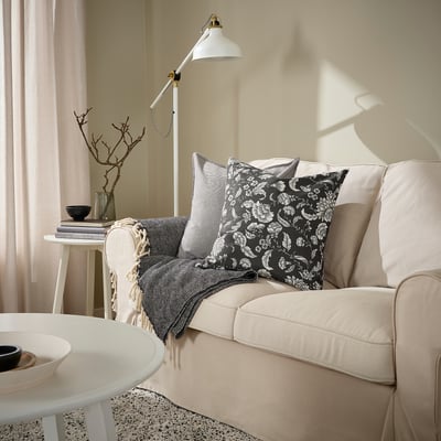 Husa de pernă idalinena cu design floral alb și negru, adăugând o senzație de prospețime canapelei. Dimensiunea sa completează decorul înconjurător.