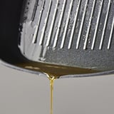 Prim-plan al uleiului auriu care picură din tigaia antiaderentă.