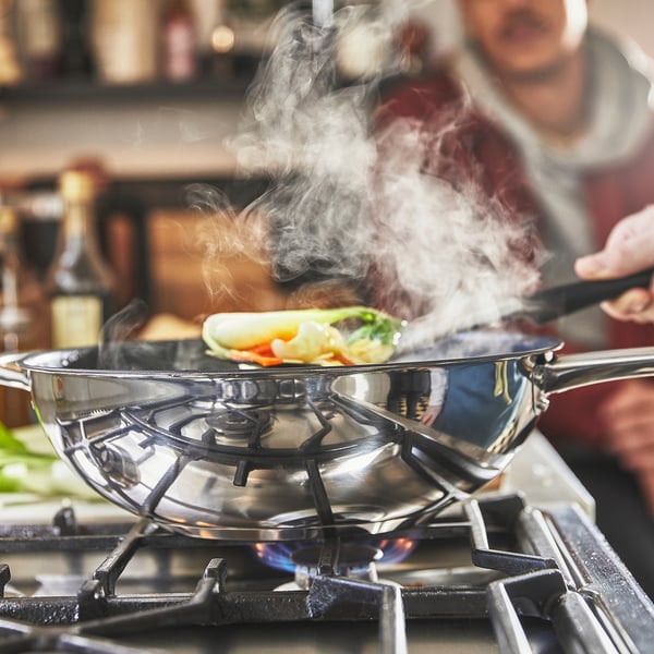 Într-un wok din oțel inoxidabil cu acoperire antiaderentă gătește mâncare colorată pe o sobă cu gaz, emițând abur.