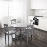 Masă rotundă extensibilă cu 4 scaune, frunze depozitate dedesubt, lângă bucătărie modernă cu cuptor.