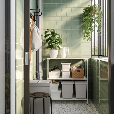 Baie modernă cu pereți din gresie verde și rafturi de depozitare albe care conțin recipiente și plante, sporind curățenia și organizarea.