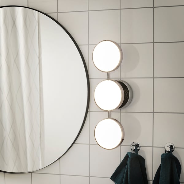 Oglindă de baie modernă cu iluminare reglabilă. Trei lumini rotunde lângă o oglindă rotundă mare. Prosoape întunecate atârnă dedesubt pe prosoape.