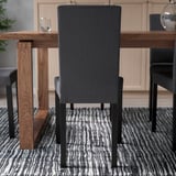 Scaun tapițat gri închis cu spătar înalt și picioare metalice împinse sub masa din lemn, potrivit pentru mese confortabile.