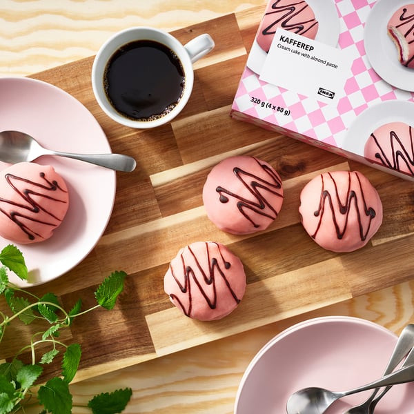 Kit coffee break: prăjituri cu cremă roz congelate, ceașcă de cafea, linguri, pe placă de lemn, cu ambalaj ikea.