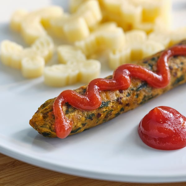 O farfurie cu un cârnat acoperit cu KETCHUP roșu și bucăți de ananas.