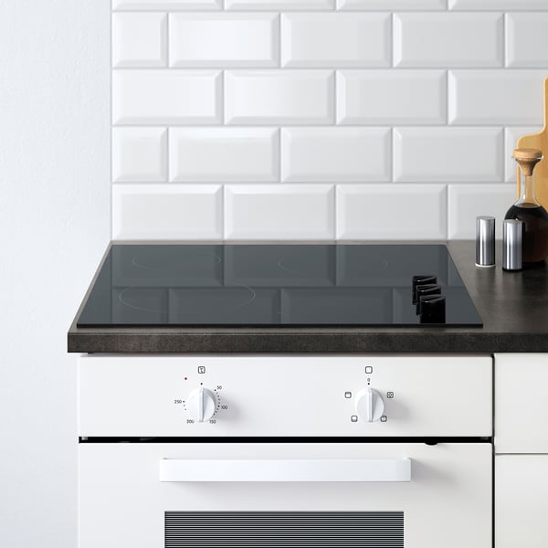 Configurație modernă de bucătărie cu aragaz modular KNOXHULT alb și butoane de control, cu o plită elegantă cu inducție din sticlă neagră.