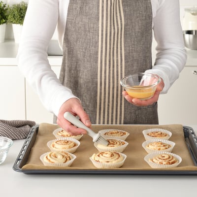 Persoana folosește o pensulă de la LÄTTBAKAD pentru a glazura produsele de patiserie pe o tavă.