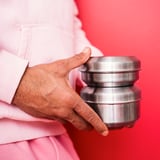 Persoană care ține un teanc de recipiente rotunde din oțel inoxidabil argintiu LÄTTUGGAD pe fundal roșu.