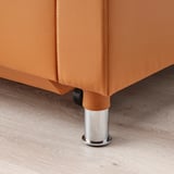 Prim-plan al unui picior de canapea din piele portocalie, textură netedă și finisaj cromat.