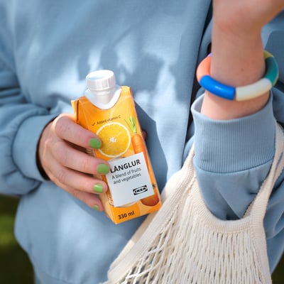 Persoană care ține în mână ikea LÅNGLUR smoothie, pulover albastru deschis, brățară cu mărgele.