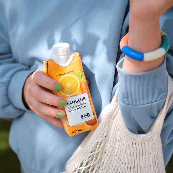 Persoană care ține în mână ikea LÅNGLUR smoothie, pulover albastru deschis, brățară cu mărgele.