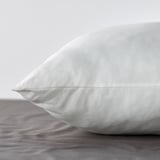 Prim-plan al unei perne albe pufoase cu țesătură netedă și texturată pe un pat.