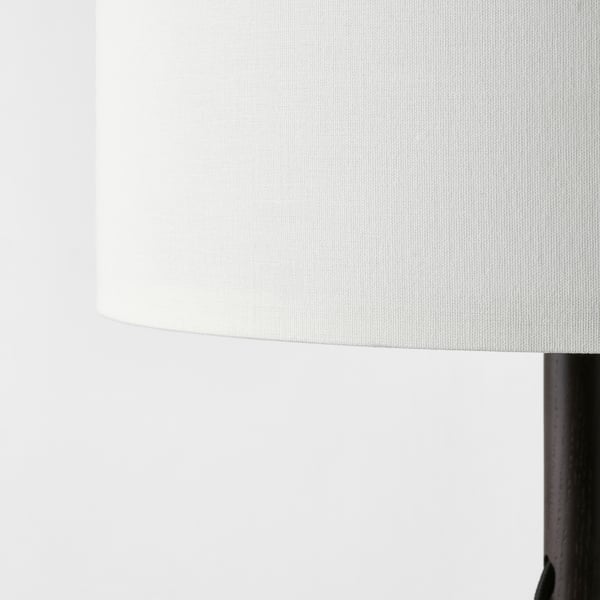 Prim-plan al unei lămpi elegante și moderne, cu un abajur alb texturat și o bază întunecată și robustă.