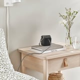 Organizator de cablu USB negru în formă de cub pe noptieră, cu un teanc de cărți și flori.