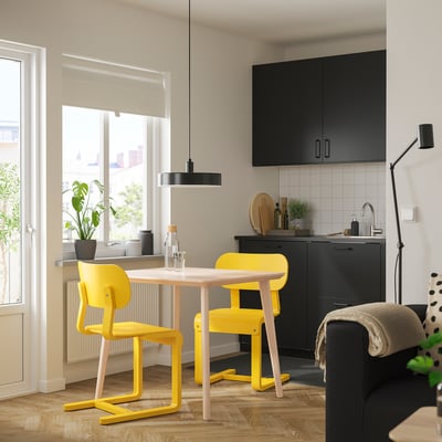 Bucătărie modernă cu set de sufragerie galben LISABO sub fereastră mare și dulapuri negre.