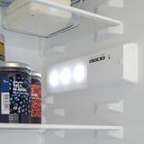 Frigider cu lumini interioare LED aprinse, care arată controlul temperaturii și recipientele.