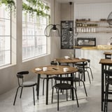 Cafenea modernă cu mese din lemn, scaune negre, plante, ferestre mari și un meniu de tablă.