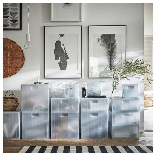 Recipiente de depozitare din plastic transparent cu capace, stivuite îngrijit. Artă abstractă pe perete, covor cu dungi alb-negru, coșuri țesute și pandantiv.