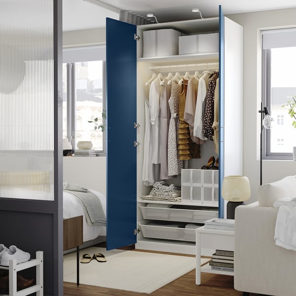 Un dormitor modern cu un dulap PAX cu model albastru deschis, dezvăluind haine și rafturi. Organizarea dulapurilor și designul interior.