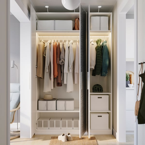 Un dressing bine organizat, cu haine pe umerase, rafturi cu coșuri și accesorii, inclusiv o pălărie și o cască.