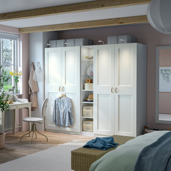 Dormitor modern cu dulap PAX alb, depozitare mixtă, cutii gri, cămașă suspendată, birou, pat, lenjerie de pat albastră, podea din lemn, lumină naturală.