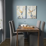 Zonă de luat masa modernă cu pereți albaștri, masă din lemn, scaune gri și două imprimeuri pe pânză de căprioare colorate.