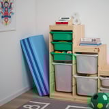 Zonă de joacă pentru copii cu covoraș albastru PLUFSIG pentru exersarea mișcărilor de gimnastică, coșuri de depozitare din lemn cu jucării și decor colorat.