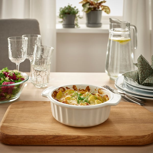 Vas mic din gresie albă pe scândură de lemn, umplut cu gnocchi și acoperit cu rozmarin. Înconjurat de pahare, farfurii și un bol de salată pe o masă.
