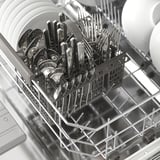 Mașină de spălat vase cu coșuri de argintărie, furculițe, linguri și cuțite.