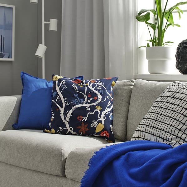 Living modern cu canapea gri, perne albastre, pătură florală, pernă cu model, verdeață, sferă decorativă argintie și lampă de podea.