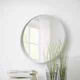 Oglinda ROTSUND pe peretele alb reflectă fereastra, planta, cărțile.