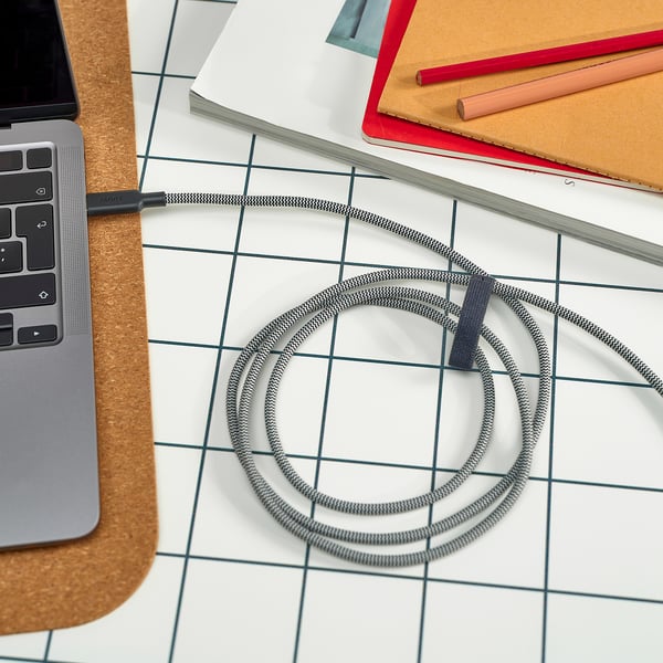 Imaginea arată un cablu de încărcare USB-C pe un birou cu un laptop și notebook-uri.